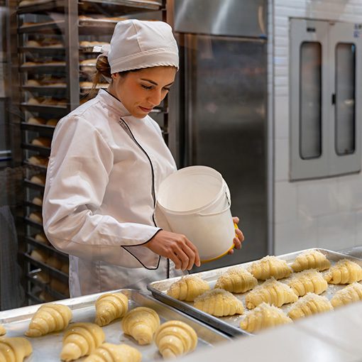 lady factory worker inspecting croissants on a conveyor belt before being cooked